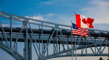 Drapeaux américain et canadien au premier plan du pont Blue Water reliant l’Ontario et le Michigan