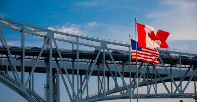 U.S. and Canadian flags wave in the foreground of the Blue Water Bridge connecting Ontario and Michigan