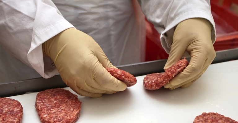 A gloved hand places raw burger patties