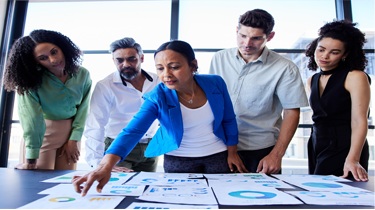 Groupe diversifié de professionnels en affaires examinant des graphiques et des tableaux économiques lors d'une discussion.