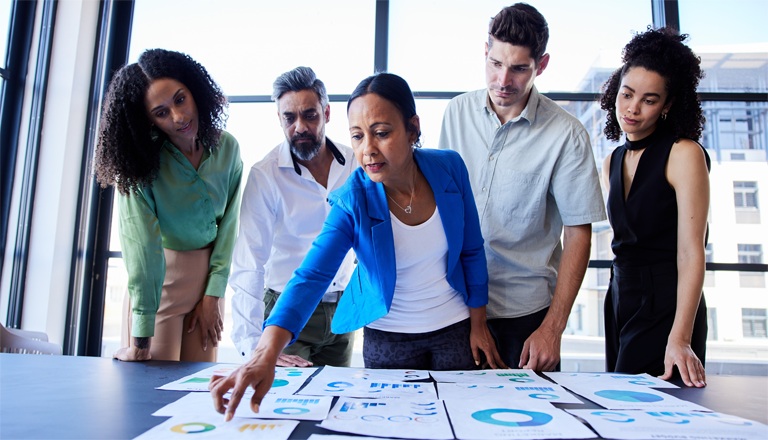 Groupe diversifié de professionnels en affaires examinant des graphiques et des tableaux économiques lors d'une discussion.