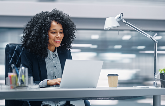Une femme noire travaille sur son ordinateur sur un bureau.