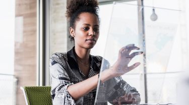 Une femme interagissant avec un écran tactile transparent tout en tapant sur un clavier dans un environnement de bureau.