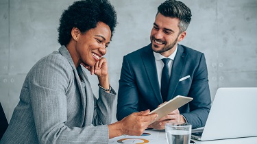 Black woman reviews her co-worker’s report on her tablet.