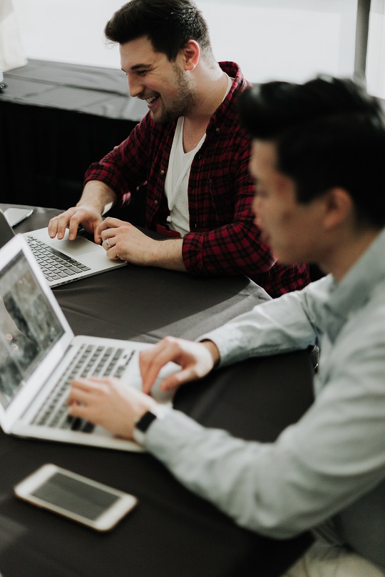 Two smiling men working on their laptops