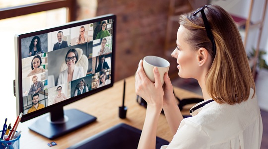 Femme assise à un bureau qui boit un café et participe à une vidéoconférence