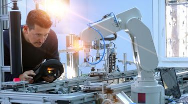 Un homme programmant un bras robotisé dans un environnement industriel à l'aide d'un panneau de commande portable.