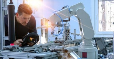 Un homme programmant un bras robotisé dans un environnement industriel à l'aide d'un panneau de commande portable.
