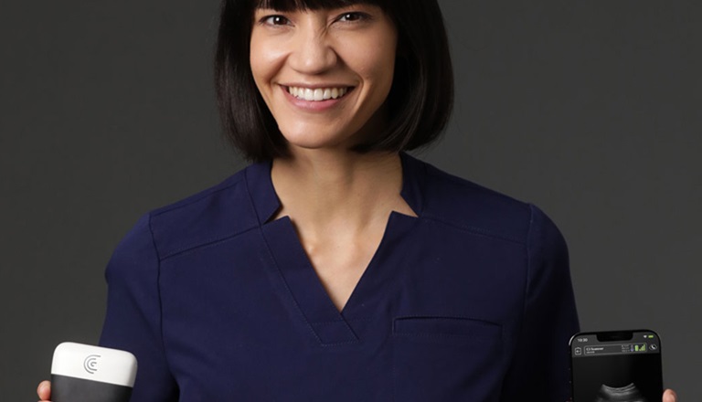 Smiling women holding Clarius portable ultrasound device in left hand and a smartphone in the right hand which shows an image of a fetal ultrasound.
