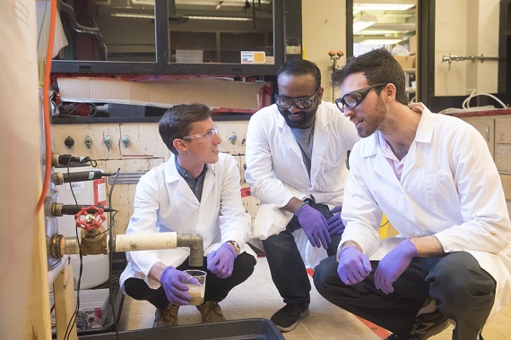 Three men in lab coats kneeling in a circle collecting a sample of upcycled food waste.