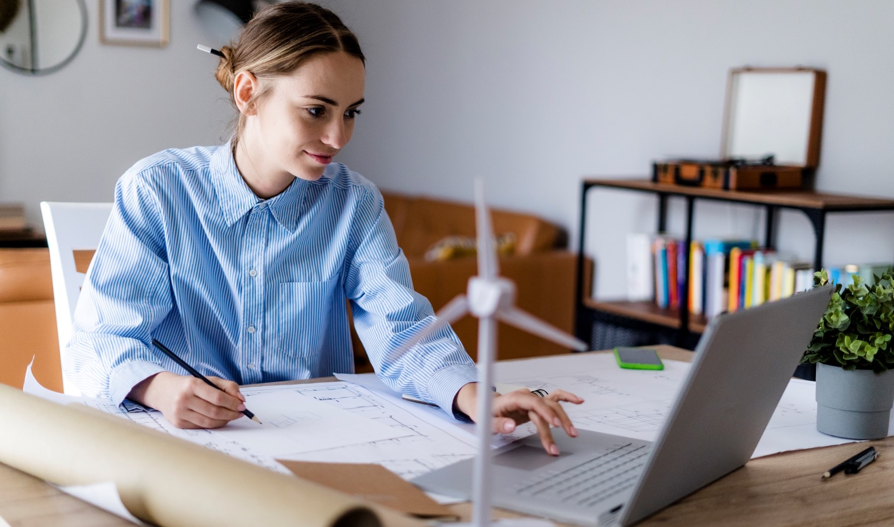  A woman sitting at her desk is typing on her computer while drafting notes on a paper