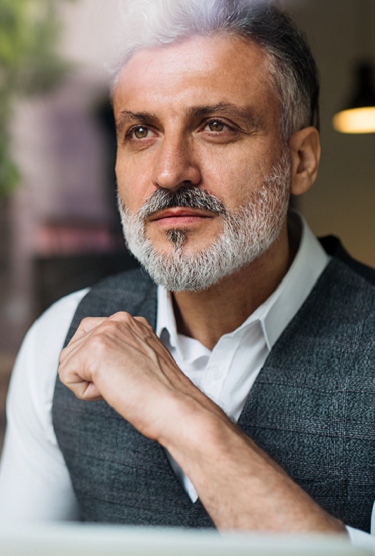 A mature exporter gazes through a window at a commercial street as he sits in a cafe.