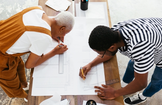 Deux architectes mettant la touche finale à un plan autour d'une table à dessin 