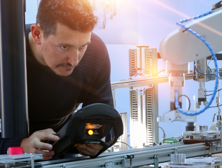 Un homme programmant un bras robotisé dans un environnement industriel à l'aide d'un panneau de commande portable.