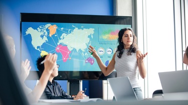 Femme d’affaires canadienne devant un écran de données affichant une carte du monde colorée avec des flèches.