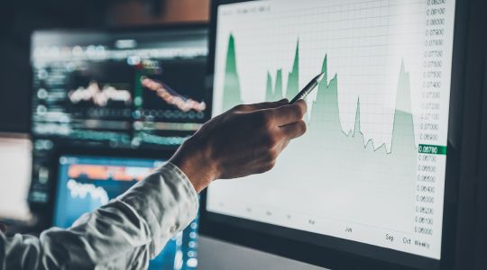 Close-up of a businessman pointing with a pen to data on a chart displayed on a computer screen.
