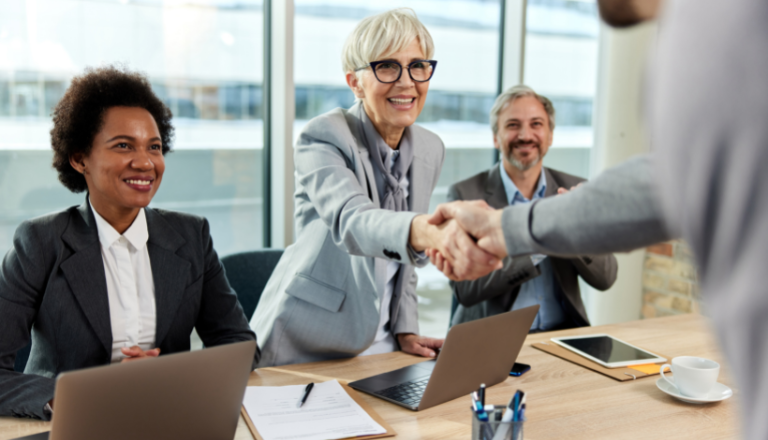 Three individual smiling and facing one other person. One of them is shaking hands with one person.