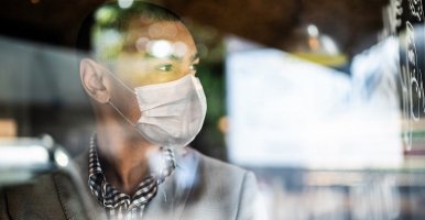 Black exporter wearing mask looks out office window