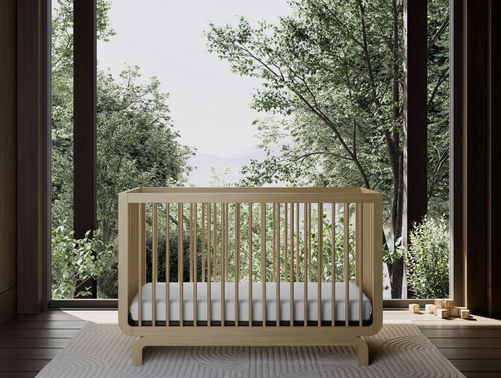 Un lit de bébé minimaliste en bois dans une pièce lumineuse dotée de grandes fenêtres et avec des arbres à l’extérieur
