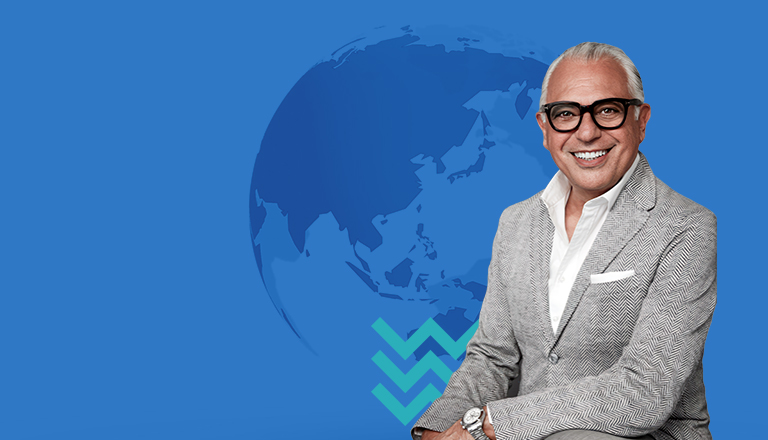 Joe Mimran poses with globe with blue chevrons in background.