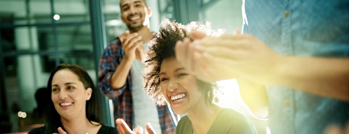 Work colleagues (men and women) smile and clap their hands to celebrate their company’s success.