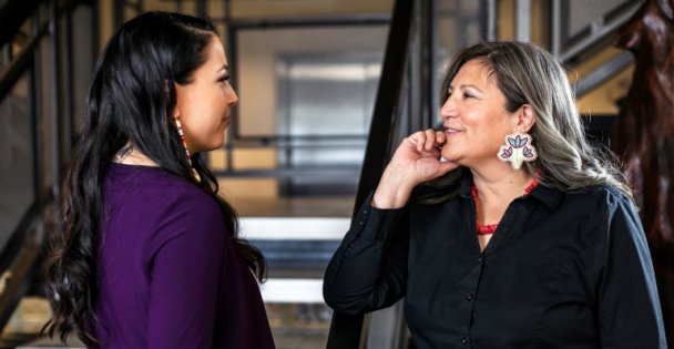 Two Indigenous women have a conversation in an office lobby. 