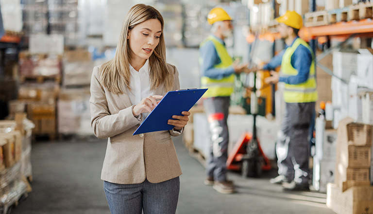 Female warehouse manager checking product on aisle in warehouse factory