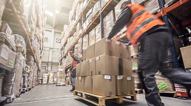 Deux travailleurs déplacent une grande palette de boîtes dans un entrepôt.