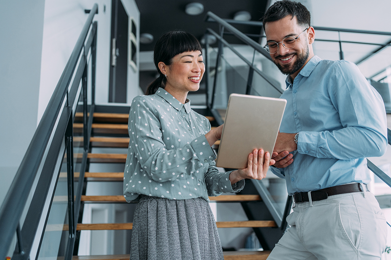 Two colleagues standing on an office staircase looking at a digital tablet.
