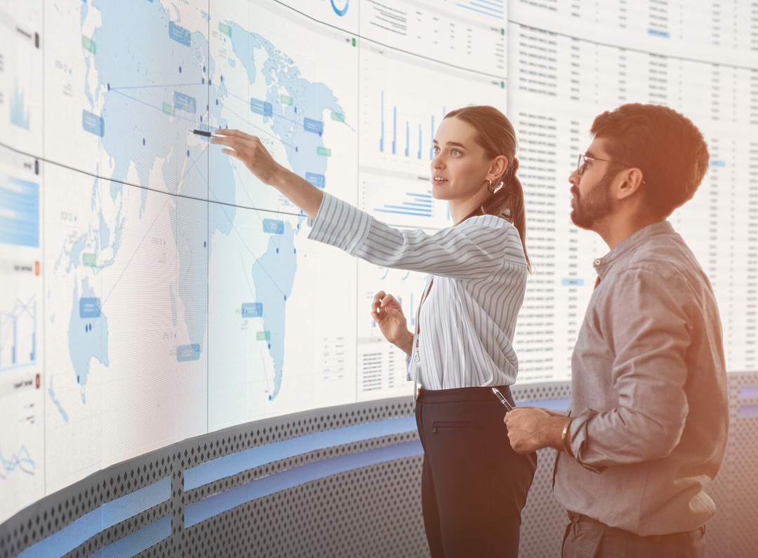 Two people reviewing international markets on a large digital world map.