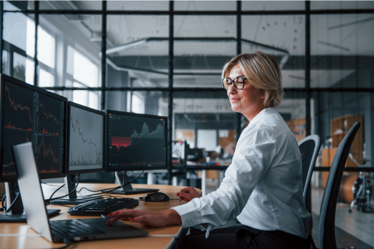 A woman looking at financial metrics across multiple computer screens.