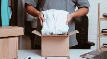 Close-up of hands placing clothes in a cardboard box in an inventory room.