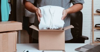 Close-up of hands placing clothes in a cardboard box in an inventory room.