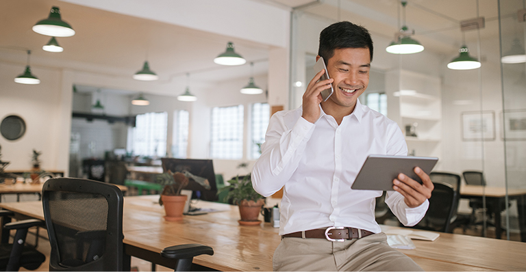 “A smiling businessman confers with his colleagues using a phone and a tablet”