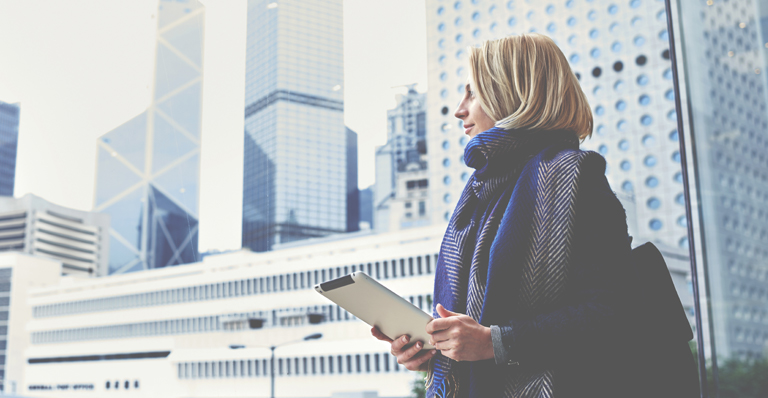 "Une femme d’affaires, tablette à la main, regarde par la fenêtre l’activité extérieure dans les rues de Hong Kong."