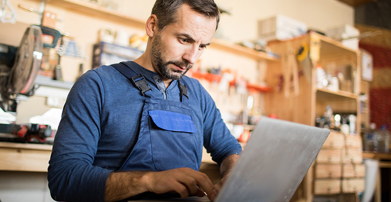 A worker is using a laptop in a carpenter’s workshop interior.