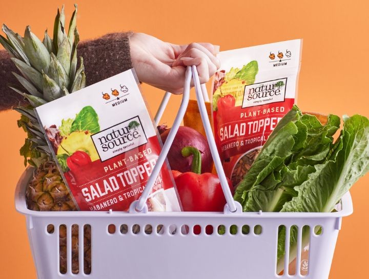 Une main tenant un panier rempli de produits frais et de produits alimentaires d’origine végétale