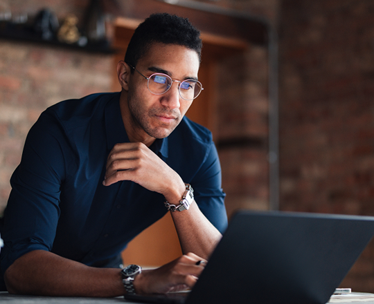Un homme d'affaires effectue des recherches sur les risques commerciaux sur un ordinateur portable dans un bureau moderne aux murs en briques.
