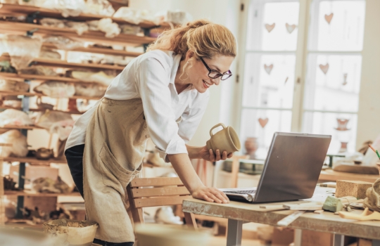 Potter entrepreneur using laptop in workshop