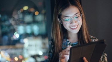 A woman is smiling while looking at her tablet