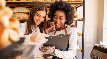 Young female bakery owners smile while accessing iPad.