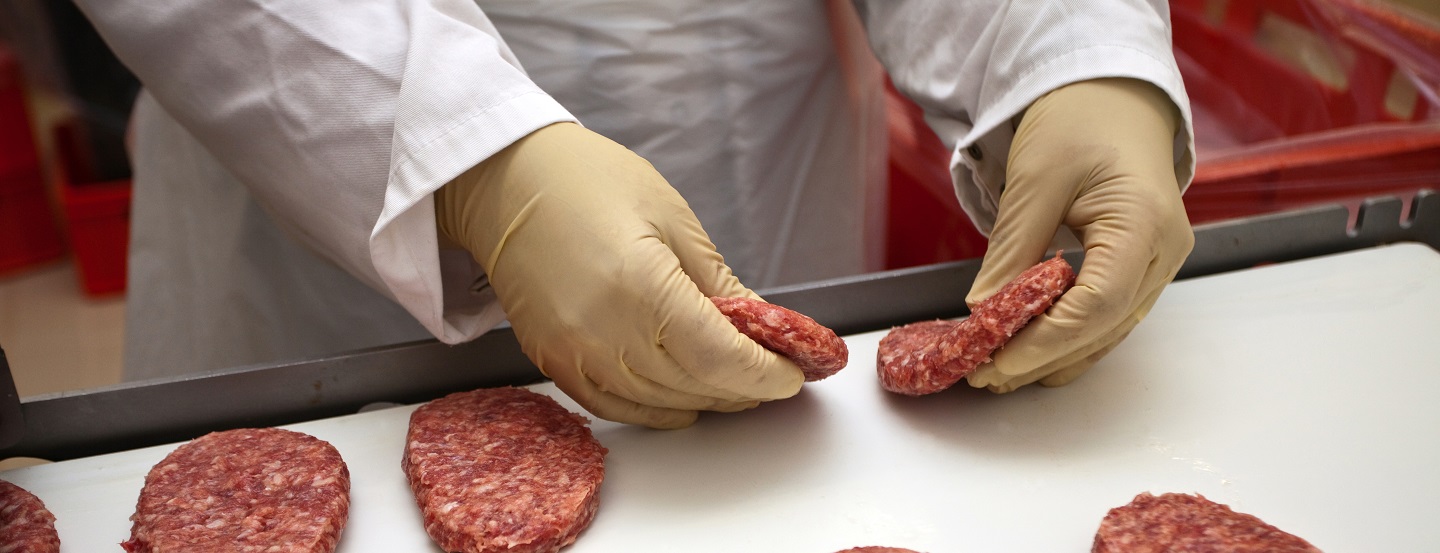 a gloved hand places raw burger patties