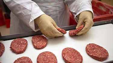 a gloved hand places raw burger patties