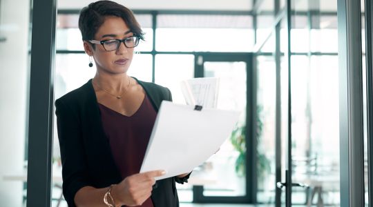A businesswoman in professional attire examining documents in an office setting.
