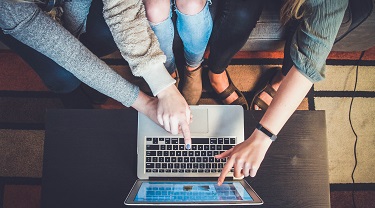 Three entrepreneurs gather excitedly around a laptop to see their new online store.