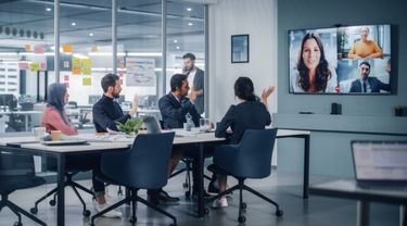 Business meeting with participants in an office and others joining by video conference.