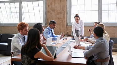 Female manager leans while addressing team at board meeting