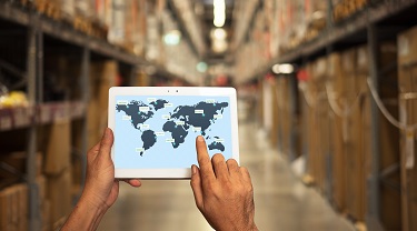 Man in a warehouse with tablet showing the map of the world where the goods will be delivered. 