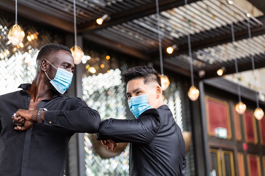 Deux hommes d’affaire portant un couvre-visage, se saluent en respectant les directives de COVID-19 