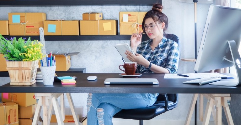 A woman sitting at her desk is reading notes from a book